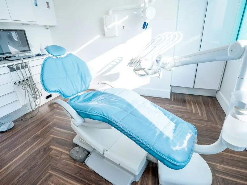 Consultorio con sillón odontológico celeste, lámpara de techo y piso de madera