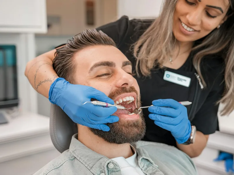 Higienista realizando una limpieza dental a un paciente recostado en el sillón